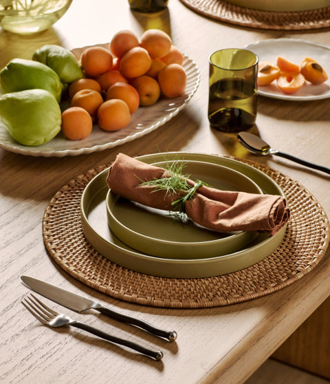 Table setting with green plates, brown napkin, and fruit.