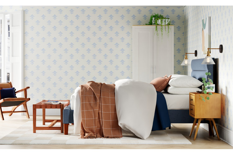 eclectic bedroom with blue patterned wallpaper, white-and-brown bedding, and a blue upholstered bed frame