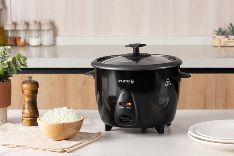 black rice cooker next to a small wood bowl full of cooked rice