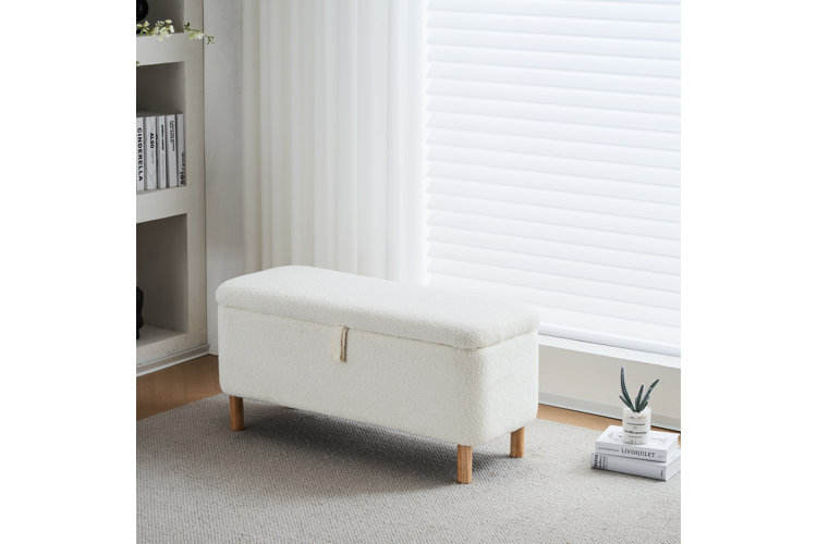 A long rectangular storage bench upholstered in cream-colored bouclé fabric with natural light wood tapered legs and a lift-top lid