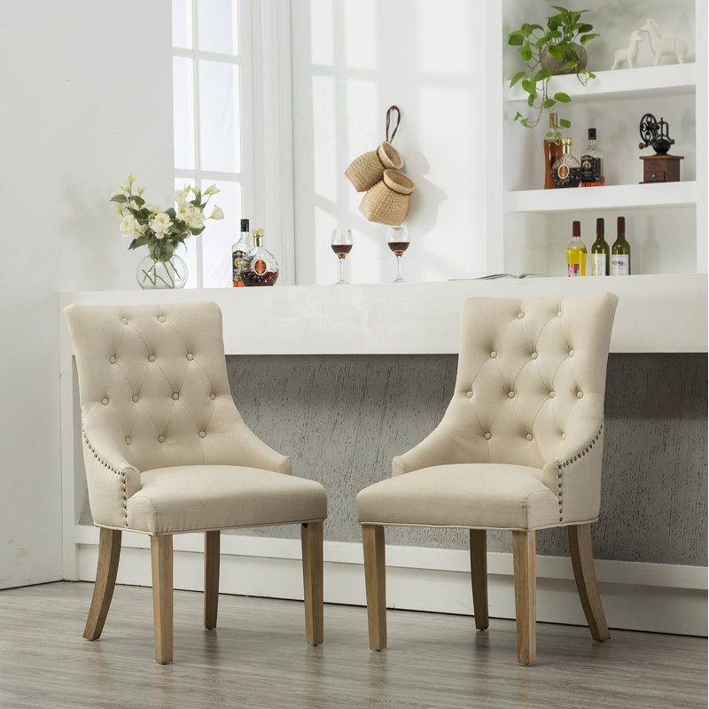 Ensemble de deux fauteuils à oreilles capitonnés en bois massif brun clair avec têtes de clous, pour un siège confortable et élégant