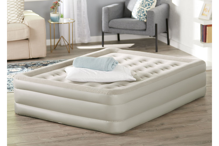 A beige air mattress with a pillow and blanket on top, placed on the floor in a living room.