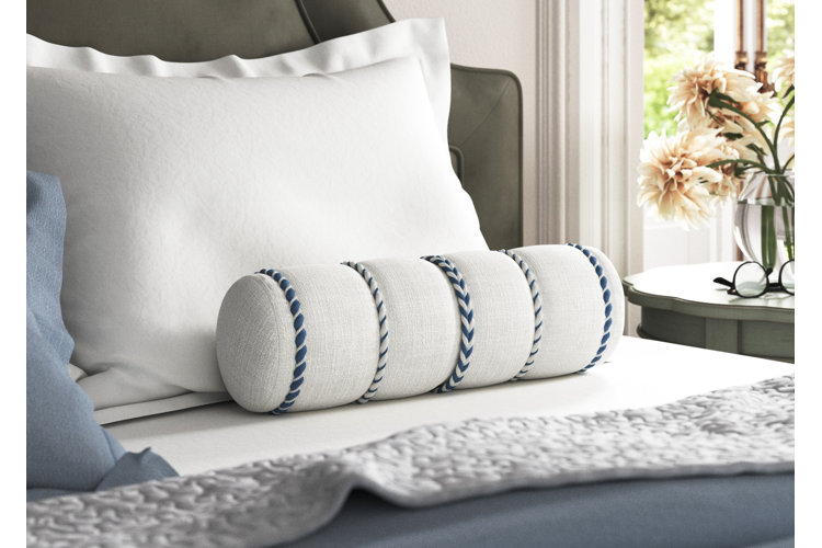 white bolster pillow with blue stitching on a bed with white sheets