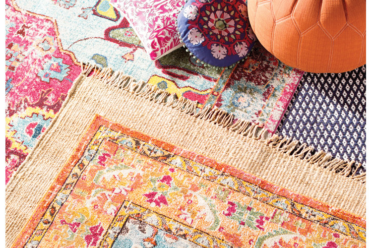 brightly colored boho area rugs layered under a set of throw pillows and an orange pouf