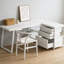 Bureau multifonctionnel blanc en forme de L pour optimiser l'espace. Il comprend 2 petits tiroirs, 1 grand tiroir, des tablettes ouvertes, un plateau en panneaux de particules et des pattes réglables. Parfait pour un bureau à domicile ou un espace de travail.