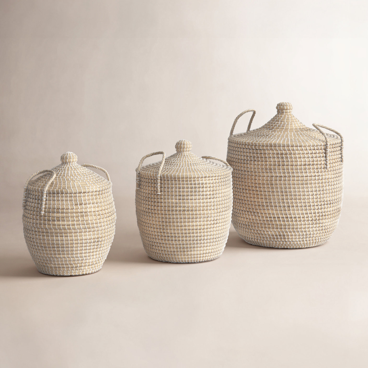 Three beige seagrass lidded baskets with rope handles in graduated sizes.
