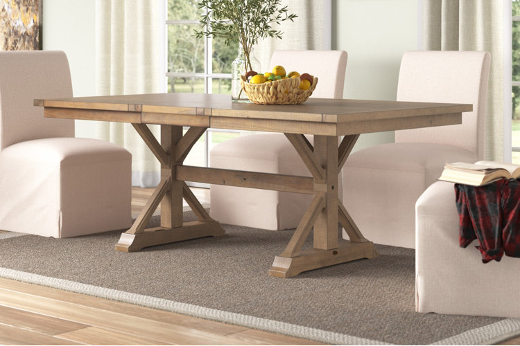 rectangular wood trestle dining table with upholstered chairs in bright dining room