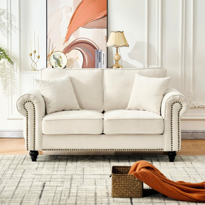 Canapé 2 places beige moderne avec accoudoirs arrondis, revêtement en chenille, pieds en bois et finis cloutés, idéal pour les appartements. Garnissage en mousse haute densité, toucher velours doux, structure en pin massif, courbé, taille moyenne.