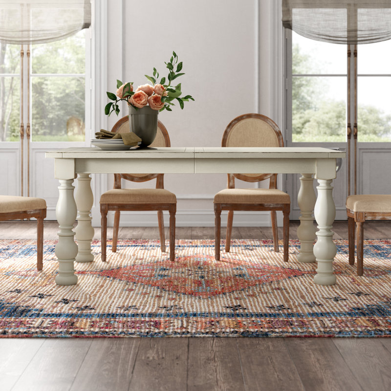 Rustic dining table with a floral arrangement, wooden chairs, and soft natural light streaming through large windows.