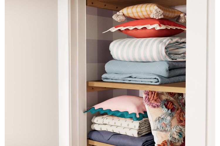 An open linen cabinet with organized stacks of bedding and throw pillows on each shelf.