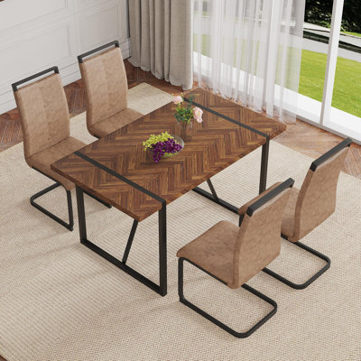 Ensemble de table et de chaises. Une table de salle à manger rectangulaire rétro avec un bureau en panneau de fibres à densité moyenne à motif en arête de poisson et des pieds en métal noir. Assorti de 4 chaises en tissu brun avec des pieds arqués noirs.