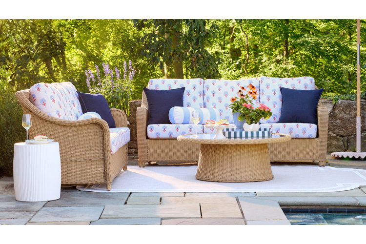 Outdoor patio furniture set conversation set with light brown wicker furniture and blue and white weather-proof cushions on a patio surrounded by greenery