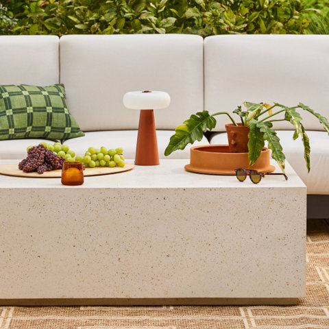 Outdoor seating area with a stone coffee table, grapes, lamp, and potted plant