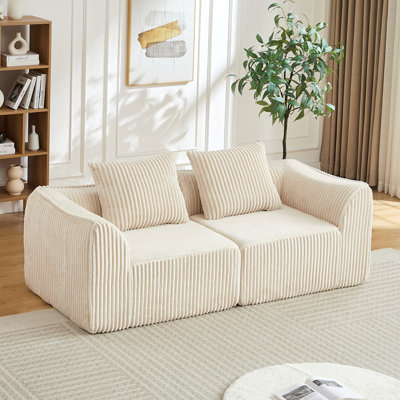 Canapé minimaliste en velours côtelé aux lignes courbes et au dossier légèrement incliné, livré avec deux coussins décoratifs, coussin décoratif en forme de corne beige