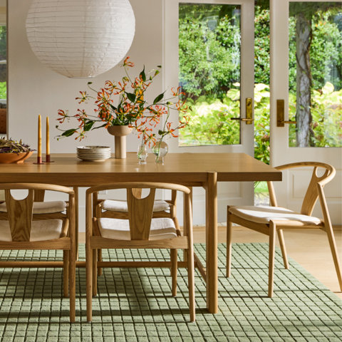 Dining room with wooden table and chairs, green rug, and outdoor view.
