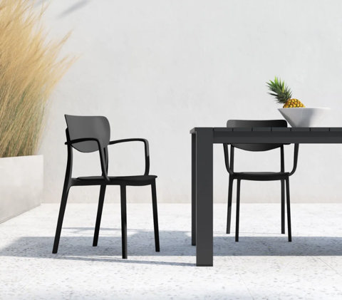 Modern black outdoor dining chairs and a matching table on a white patio with a bowl of pineapple and tall ornamental grass.