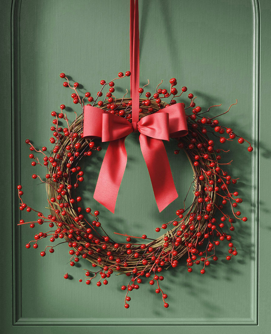 Couronne de baies avec un ruban rouge sur une porte verte.