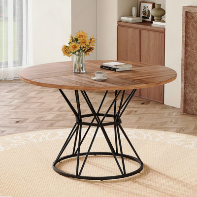 Une table de salle à manger circulaire d'un diamètre de 47,3 pouces, comprenant 4 plateaux de table en bois aggloméré à grain de bois de noyer, des supports en métal en forme de sablier noir et une table de salle à manger de style industriel moderne pour 4 à 6 personnes.