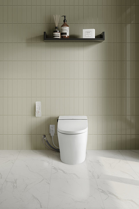 Modern white smart toilet with remote control mounted on a sage green tiled wall above a marble floor.