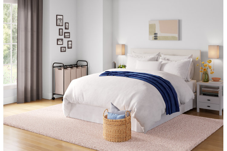 Bedroom with a double bed, white bedding, a pastel pink rug, and a laundry sorter in the corner.