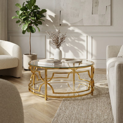 Table basse ronde moderne avec plateau en verre trempé et structure géométrique en métal doré, avec tablette de rangement inférieure