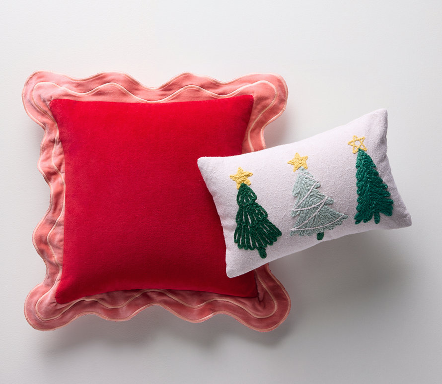 Deux oreillers décoratifs, un carré rouge et un lombaire blanc avec des sapins de Noël brodés.