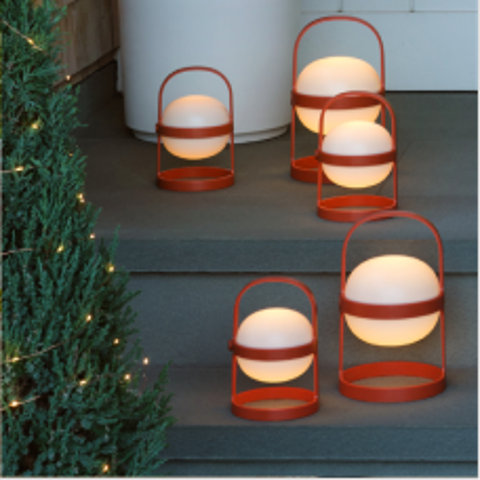 Five spherical, glowing lanterns with orange metal frames and handles arranged on gray steps next to a small lit evergreen tree.