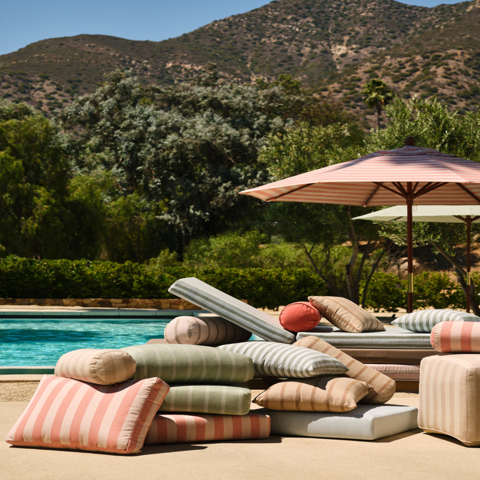 Outdoor striped pillows, loungers, and umbrellas next to a pool.