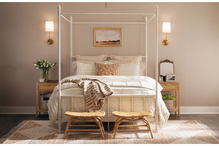 Cozy beige bedroom with a white canopy bed with white and beige bedding on top of a woven area rug with fringed ends.