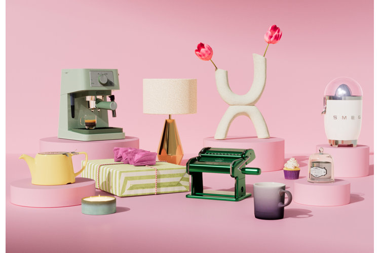 mother's day gifts in front of a solid pink background, including a pasta maker, coffee machine, a table lamp, and a vase with flowers