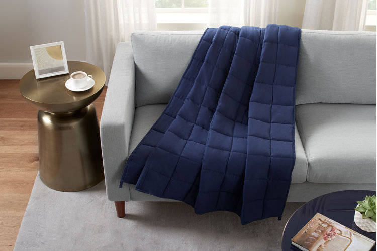 A gray couch with a blue weighted blanket draped over it and a brass end table next to the couch