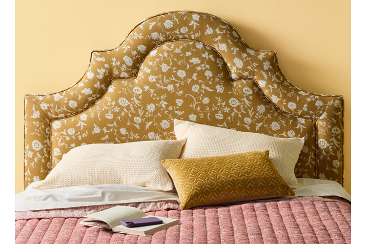 A mustard yellow floral upholstered headboard paired with coral pink bedding and yellow throw pillows