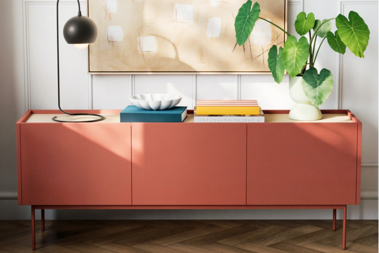 modern coral sideboard styled with black lamp, decorative bowl, stacked books, and leafy green plant