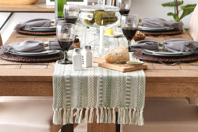 dining table set with a woven table runner, plates, wine glasses, and candles for a styled meal setting