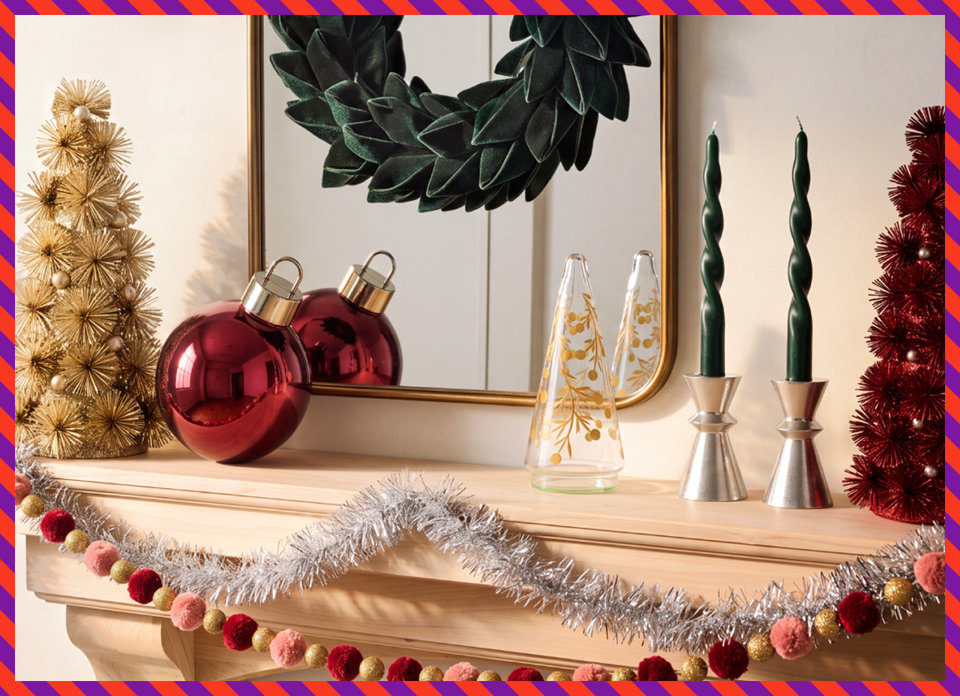 A festive fireplace mantel decorated with a gold starburst tree, a large red ornament, a glass tree, silver candle holders with dark green twisted candles, a red bottle brush tree, and a silver tinsel and pom-pom garland.