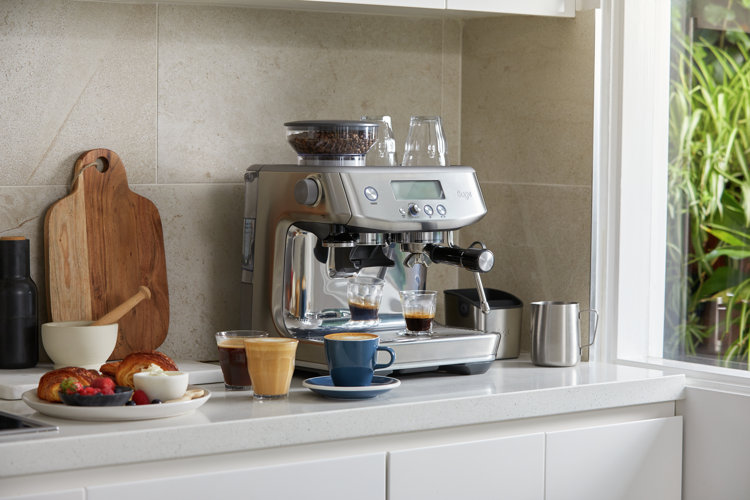 A stainless steel semi-automatic espresso machine on a kitchen counter being used to make espresso drinks.