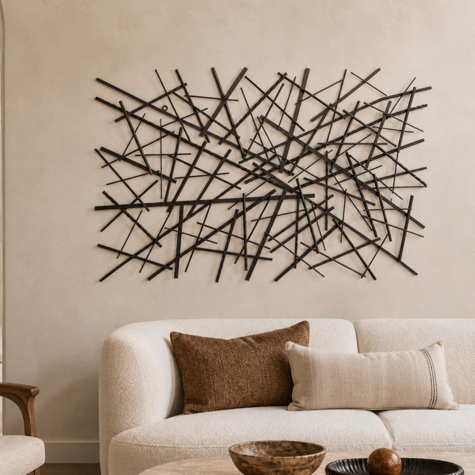 Abstract metal wall art featuring a network of intersecting thin lines displayed above a cream-colored curved sofa with textured decorative pillows.