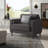 Dark gray upholstered club chair with a tufted seat, square arms, and a geometric patterned throw pillow.