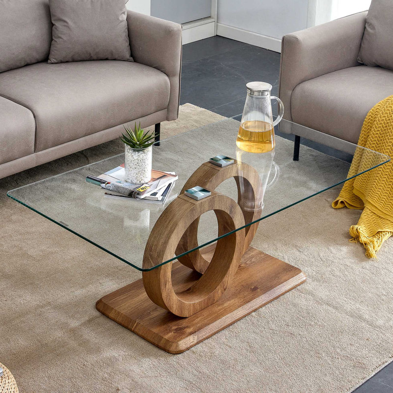 Une table basse rectangulaire moderne et tendance avec un plateau en verre trempé et des pieds en grain de bois. Convient au salon