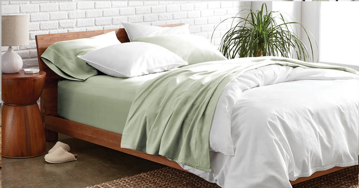A side view of a bed with light green colored sheets and a white duvet cover set