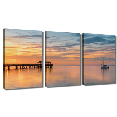 Tableau en trois panneaux représentant un voilier au coucher du soleil sur la jetée, imprimé sur une toile tendue