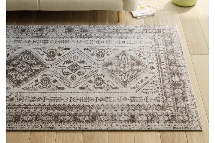 Light and dark gray Oriental-inspired area rug on a light wood floor in front of a sofa.