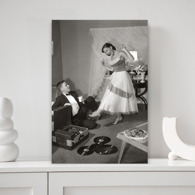1950S 1960S Teen Couple In Living Room In Prom Dress & Tuxedo Guy Sitting On Floor & Girl Dancing To Music From A Record Player Romantic Contempora...