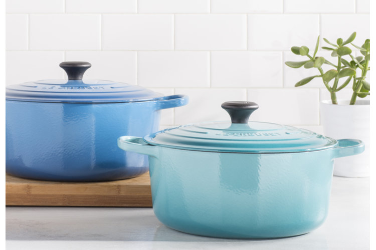 Two blue Dutch ovens on a wood cutting board