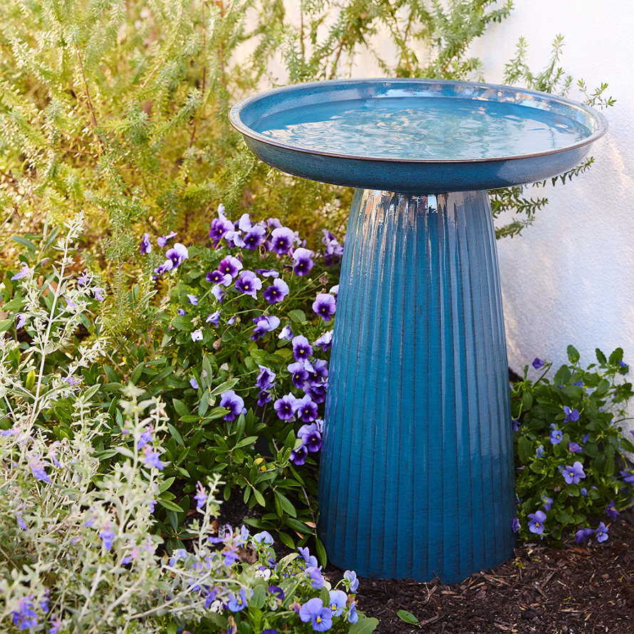 Blue bird bath surrounded by flowers and greenery.