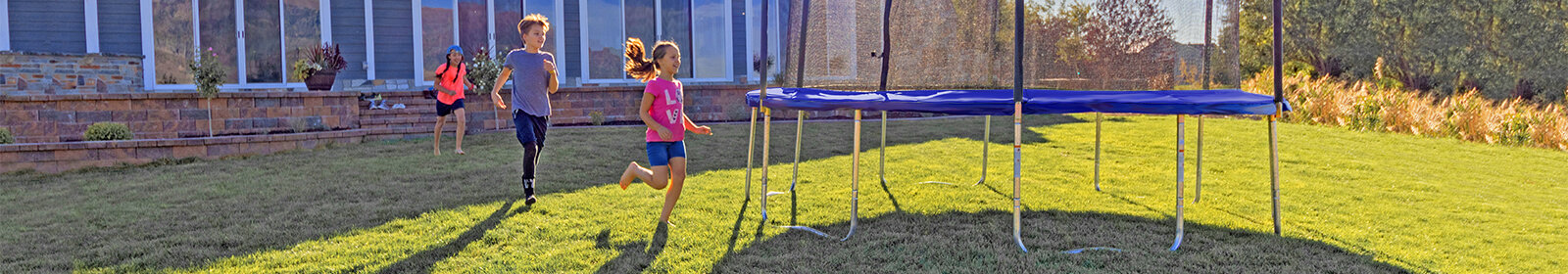 Children excitedly running towards a Skywalker Trampolines round trampoline in their backyard
