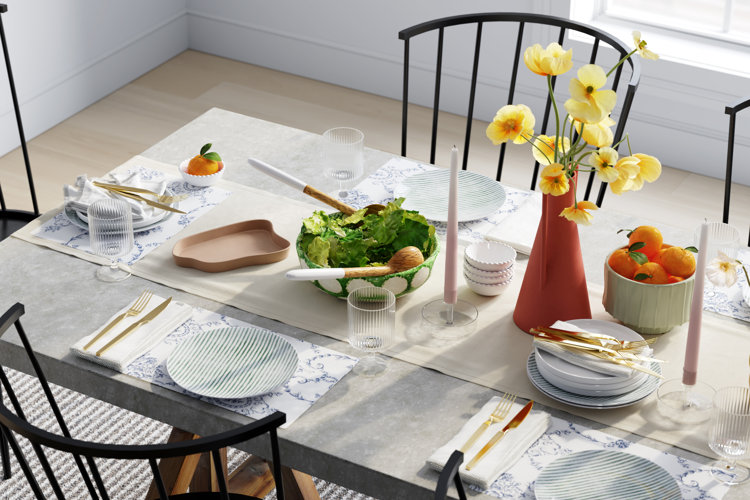 table with striped dinner plates, fluted glasses, floral placemats, and a solid-color beige table runner