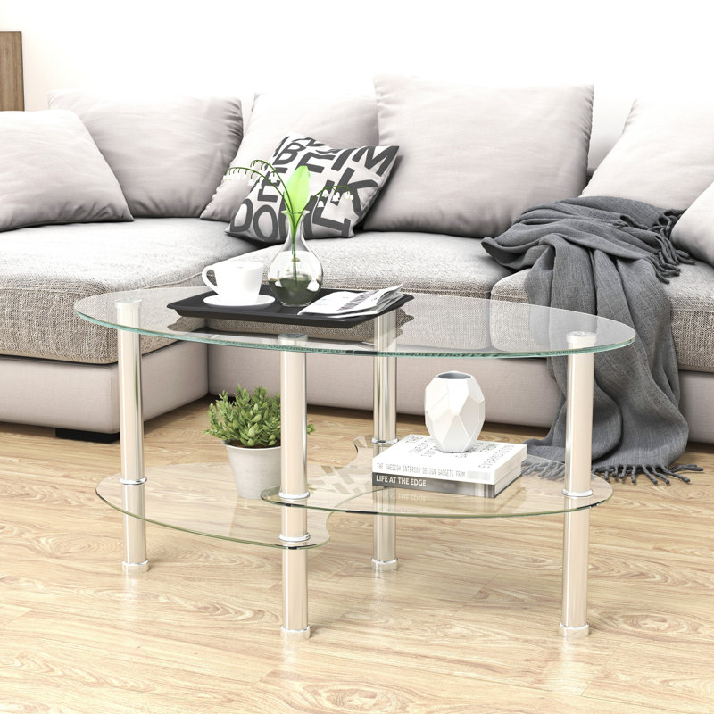 Table basse moderne en verre transparent avec pattes en acier inoxydable, de forme ovale et à trois niveaux, idéale pour le salon. Meuble polyvalent et fonctionnel.