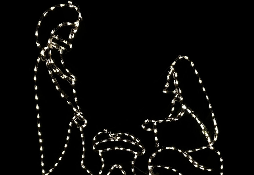 Lighted outdoor holiday silhouette of the Holy Family in a manger against a black background.