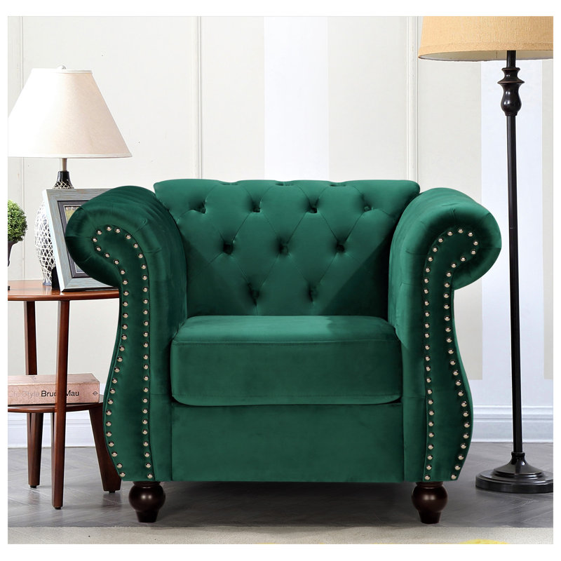 Fauteuil d'appoint Chesterfield en velours côtelé vert, avec accoudoirs arrondis, dossier capitonné, pieds fuselés en bois et coussin cylindrique assorti.